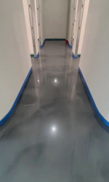 A hallway with a shiny, reflective gray floor and white walls.