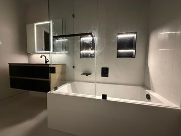 Modern bathroom with illuminated mirror and bathtub.