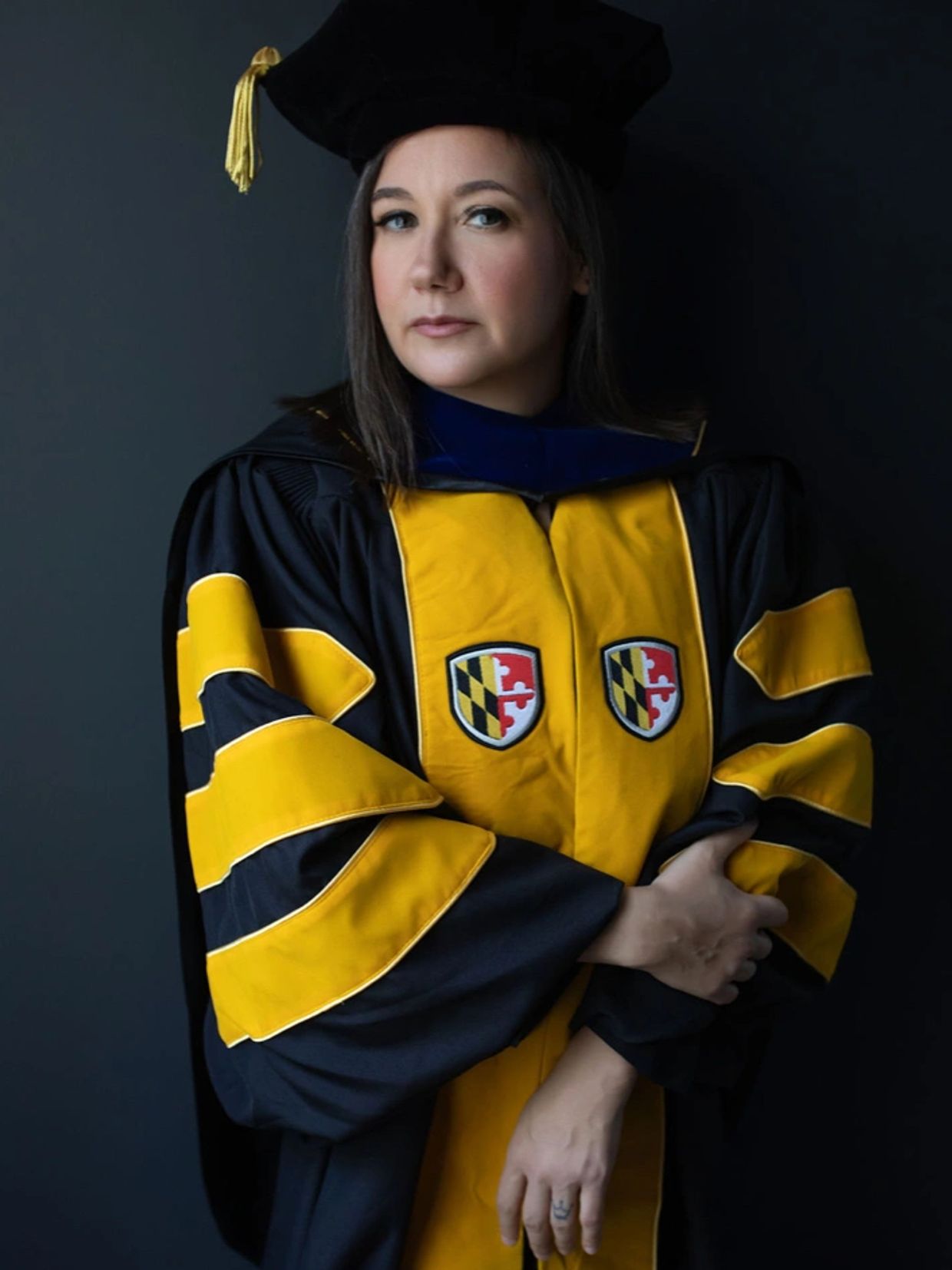 Dr. Chrissie Reilly wears doctoral regalia in the colors of UMBC. She is wearing a black robe with g