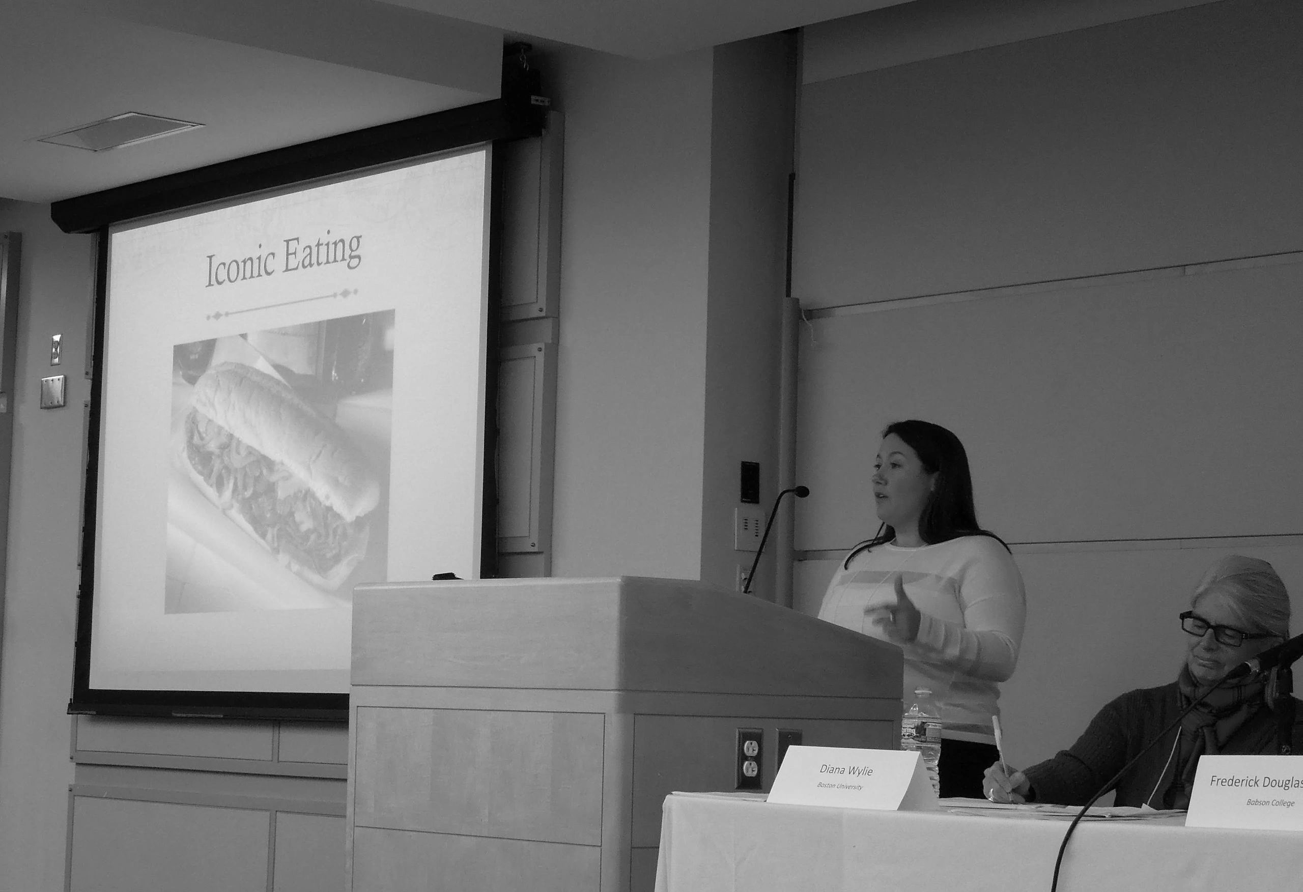 Dr. Chrissie Reilly presenting at a food studies conference about the history of the Philadelphia cheesesteak. The slide is titled 'Iconic Eating' with a sandwich image.