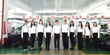Group of employees in white shirts and black pants standing in a factory setting.
