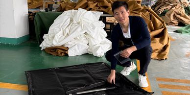 Man showcasing a black floor guard mat in a fabric workshop.
