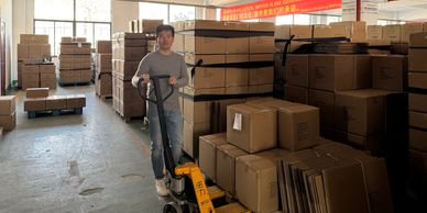 Man operating a pallet jack in a warehouse filled with stacked boxes.