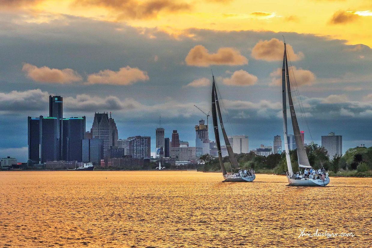 Two sailboats on a river with a city skyline at sunset.