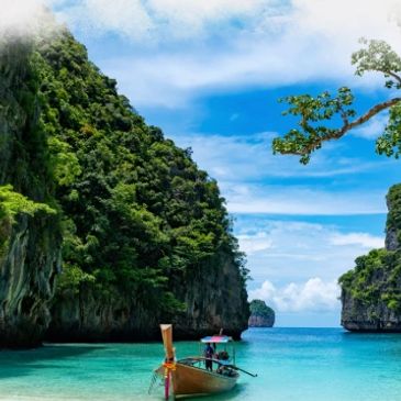 A traditional boat floats on clear turquoise water between lush green cliffs under a bright blue sky.
