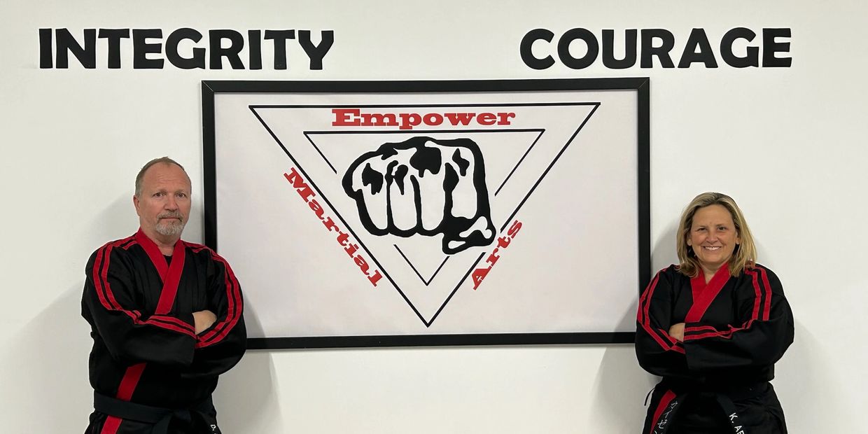 Two martial artists stand confidently by a wall with motivational words and a fist logo.