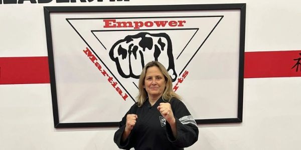 Woman in martial arts uniform posing with fists raised in front of a martial arts sign.
