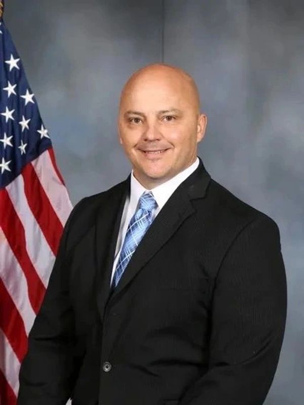 Man in a suit standing before an American flag.