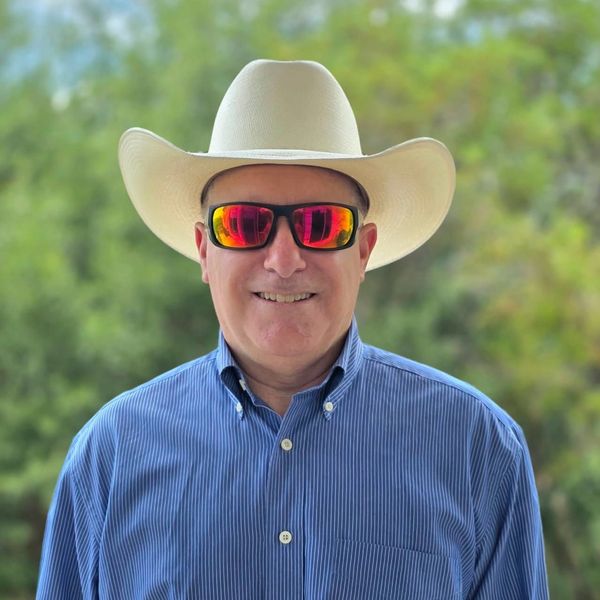 A person wearing a white cowboy hat and reflective sunglasses smiles