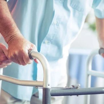 An elderly person using a walker with assistance from another individual.