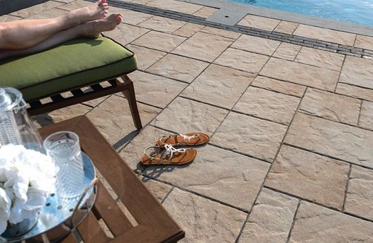 Person relaxing by the pool with sandals on the ground and a drink on a table.
