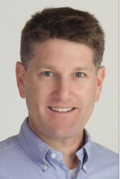 Portrait of a smiling man in a light blue collared shirt.