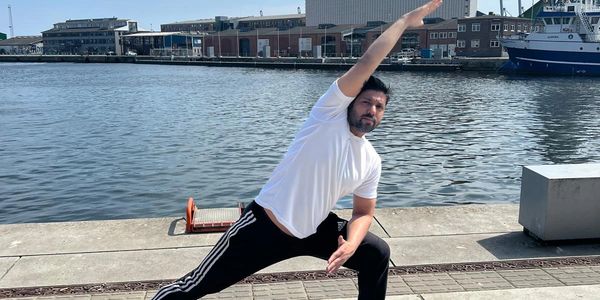 Man practicing yoga stretch by the waterfront on a sunny day.