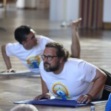 Two men practicing yoga indoors on a wooden floor.