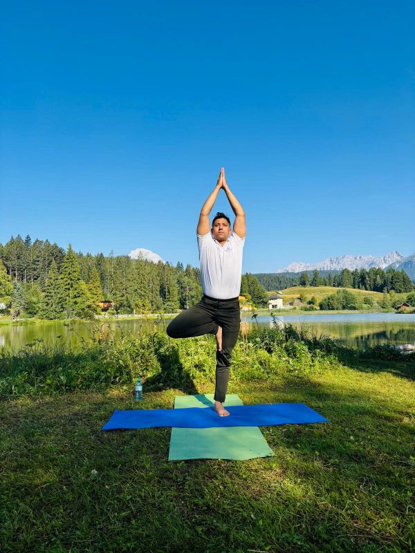 Mand udfører yoga i naturen ved en sø.