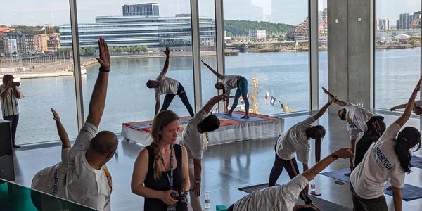 Group practicing yoga indoors with waterfront view through large windows.