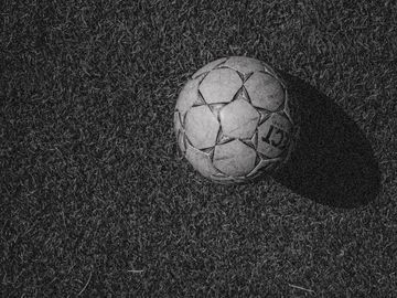 Worn soccer ball on grass casting shadow.