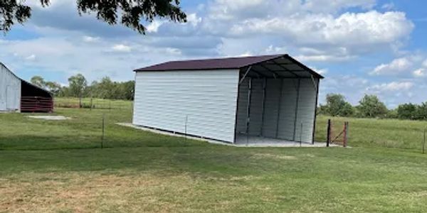 A small metal storage shed in a grassy field under a partly cloudy sky.