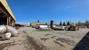 Industrial yard with large metal pipes and equipment under a clear blue sky.