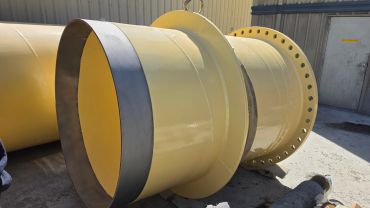 Large yellow industrial pipe segment with flange on concrete floor.