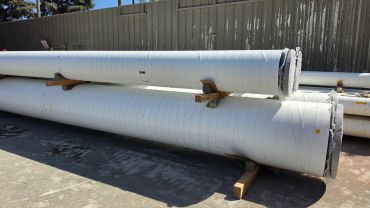 Large white industrial pipes stacked outdoors on wooden supports.