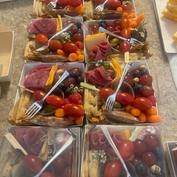 Multiple charcuterie boxes with meats, cheeses, fruits, and vegetables on a countertop.