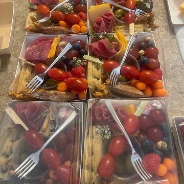 Multiple charcuterie boxes with meats, cheeses, fruits, and vegetables on a countertop.