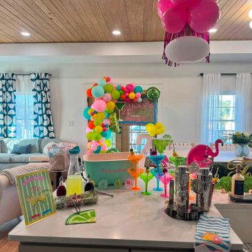 Colorful tropical-themed party setup with balloons and cocktails on a kitchen island.