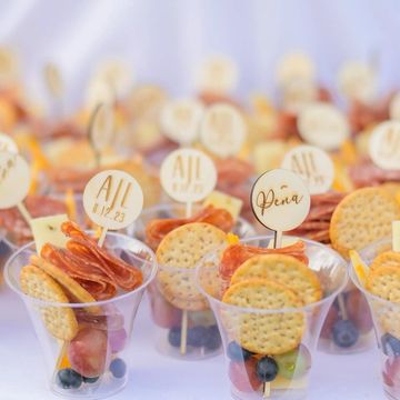 Individual snack cups with crackers, meat, cheese, and fruit, each labeled with personalized tags.