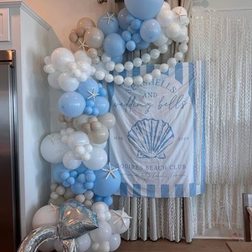 Beach-themed balloon arch with seashell decorations and a striped banner.