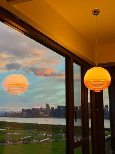 A glowing lamp inside reflects like a sunset on the window overlooking the city.