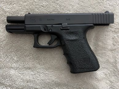 Black Glock 19 Gen 5 handgun on a textured surface.