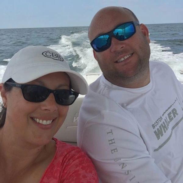 Couple enjoying a sunny boat ride on the ocean, smiling and wearing sunglasses.