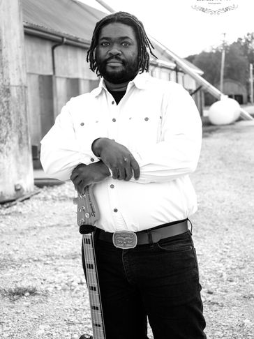 Man with dreadlocks posing with a guitar outdoors.