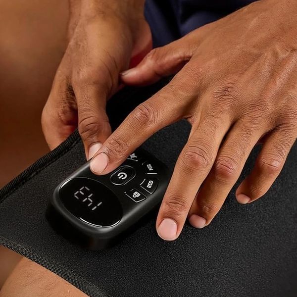 Person using an electronic knee therapy wrap with control panel.