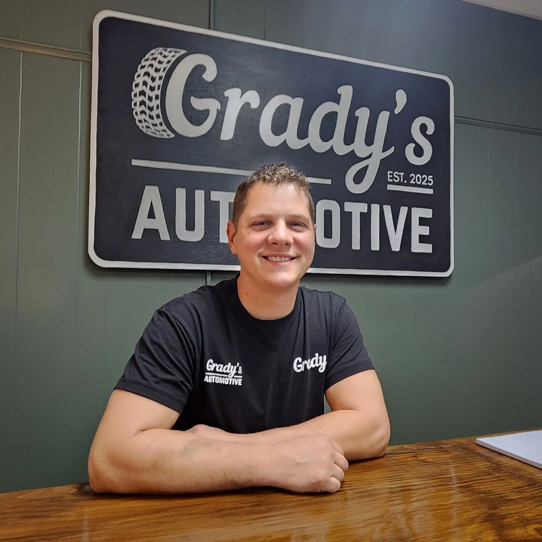 Smiling man at Grady's Automotive, wearing branded black shirt.