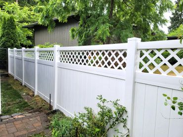 A white vinyl privacy fence with lattice top panels along a garden path.