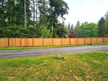 A long wooden fence along a gravel road with tall trees in the background.