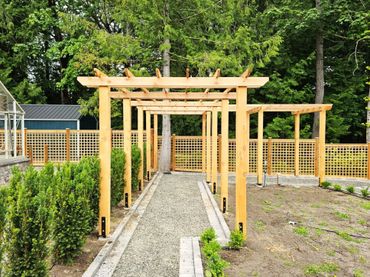 Wooden pergola with gravel path in a garden setting.