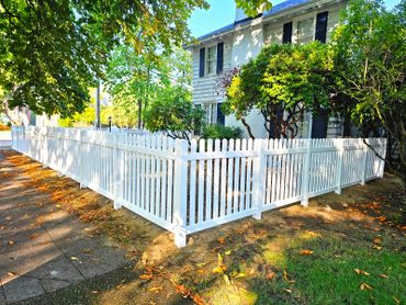 White picket fence surrounds a charming house with greenery.