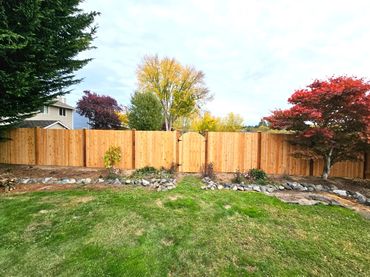 A wooden fence with a gate in a backyard with trees and grass.