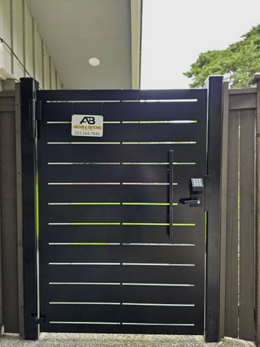 Black metal gate with keypad entry and security sign.