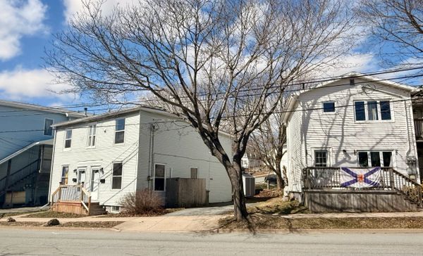 Two white houses separated by a tree and driveway under a partly cloudy sky.