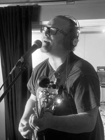 Man passionately singing and playing guitar in a studio.