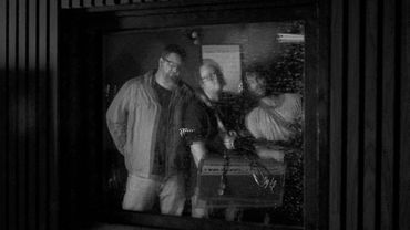 Black and white photo of two men reflected in a window.