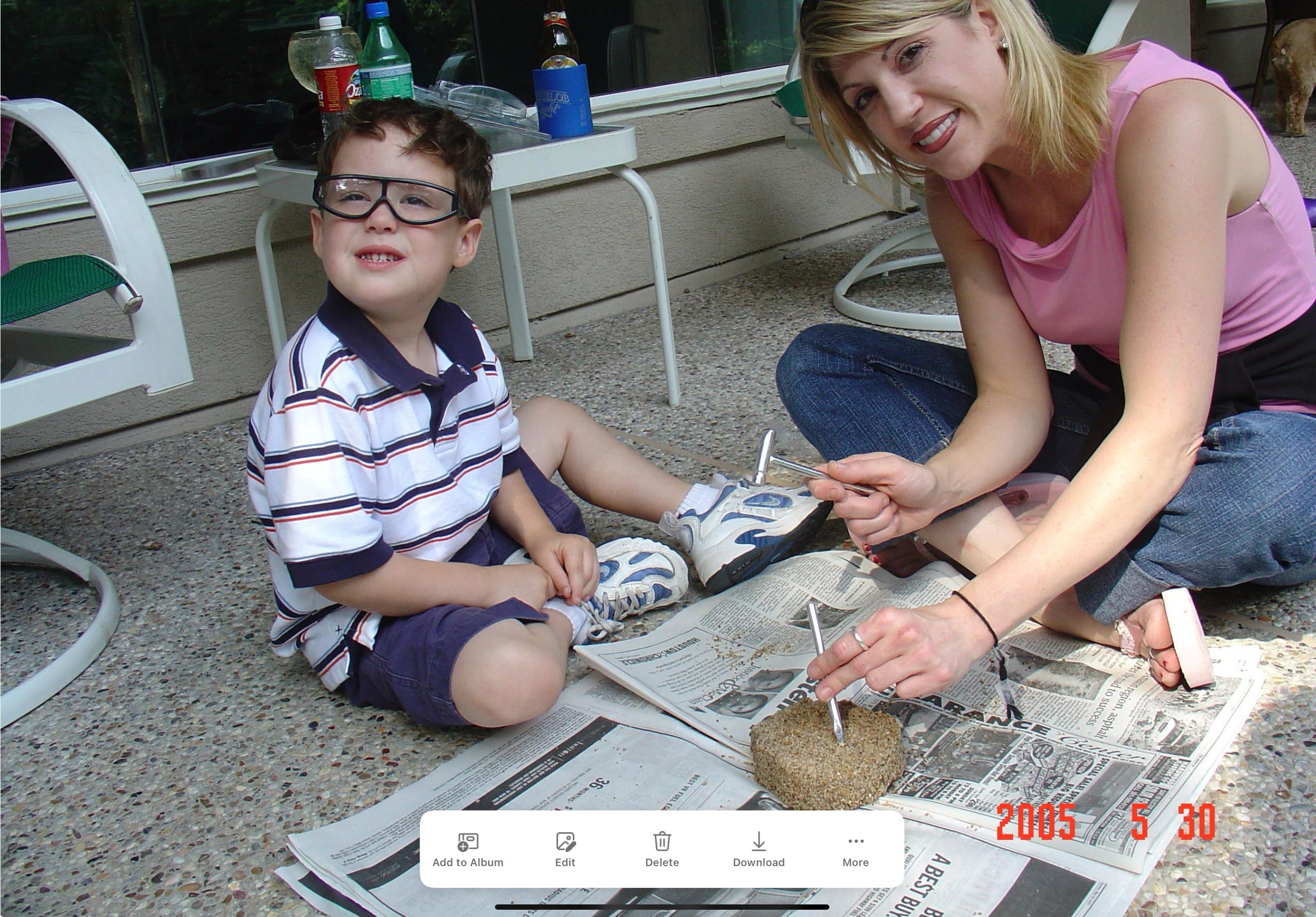Woman and child crafting outdoors on newspaper.