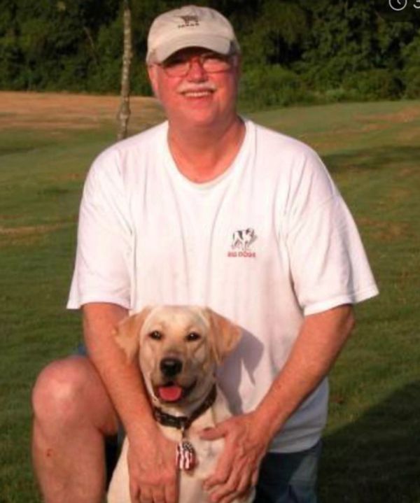 Man in white shirt with a dog outdoors.