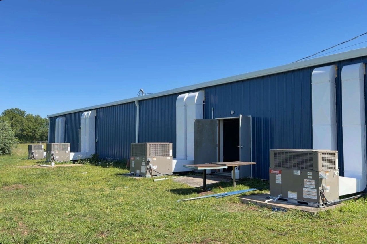Blue industrial building with HVAC units and an open door under clear sky.