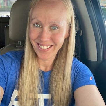 Smiling woman with long blonde hair wearing a blue shirt inside a car.