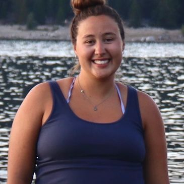 Smiling woman in a blue tank top by a lake.